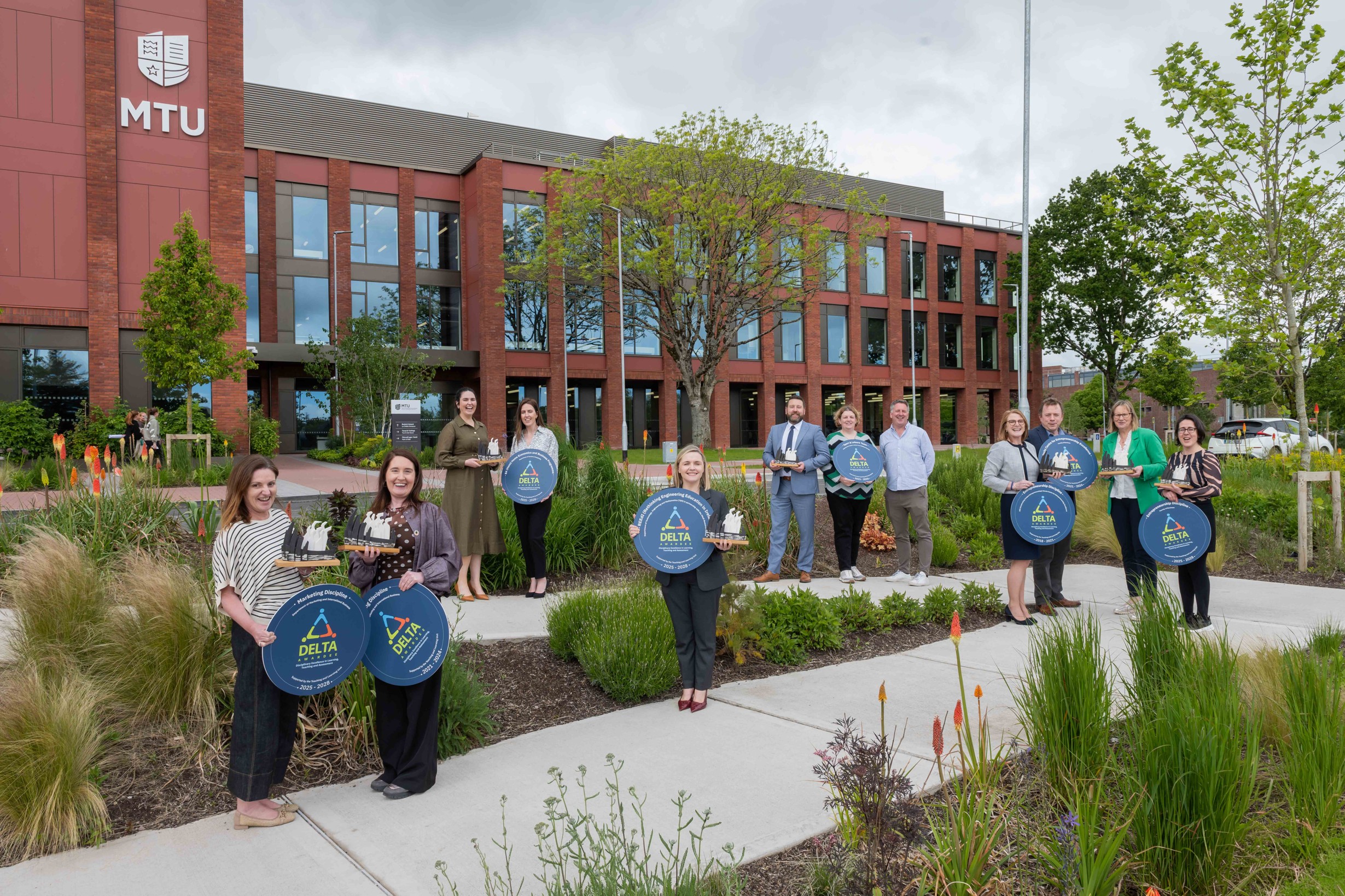 MTU staff holding DELTA Award plaques and trophies outside an MTU building